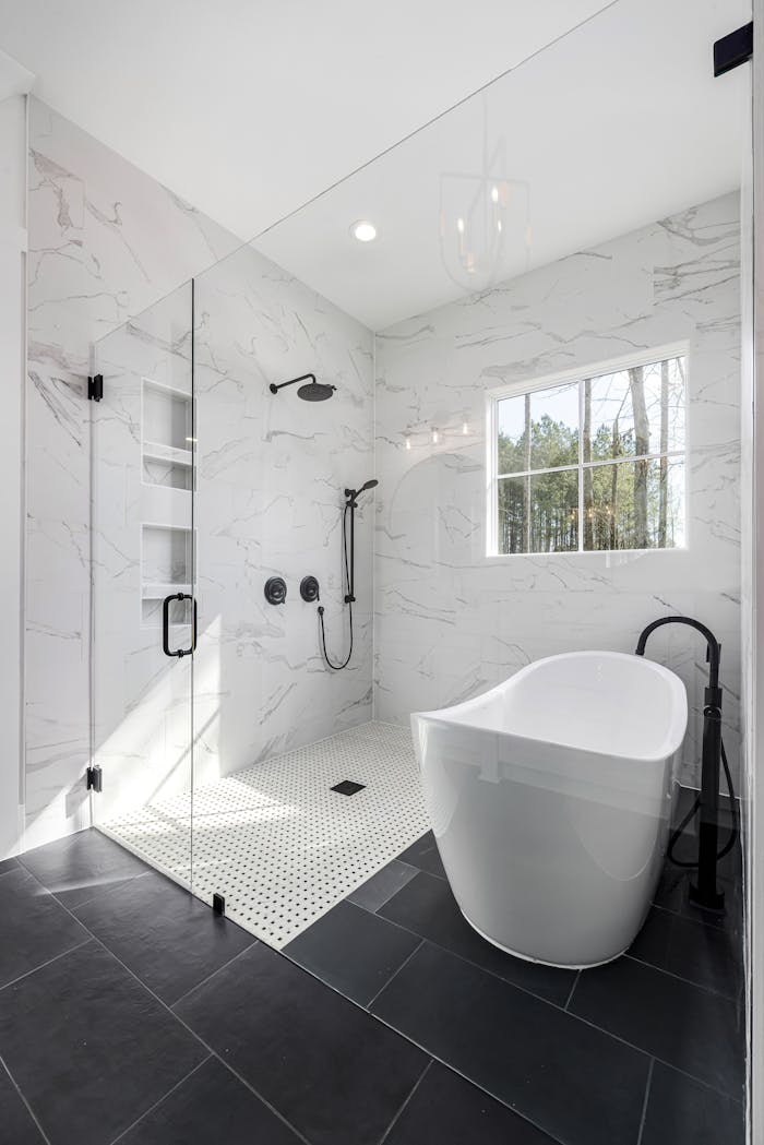 hero-img Sleek white bathroom with freestanding tub, glass shower, and natural lighting.