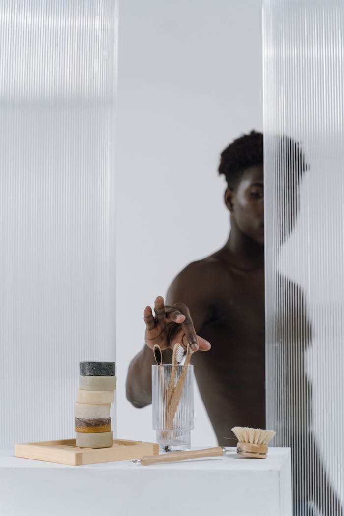 about-me-02 A man reaches for a toothbrush amidst natural soap bars in a minimalist setting.
