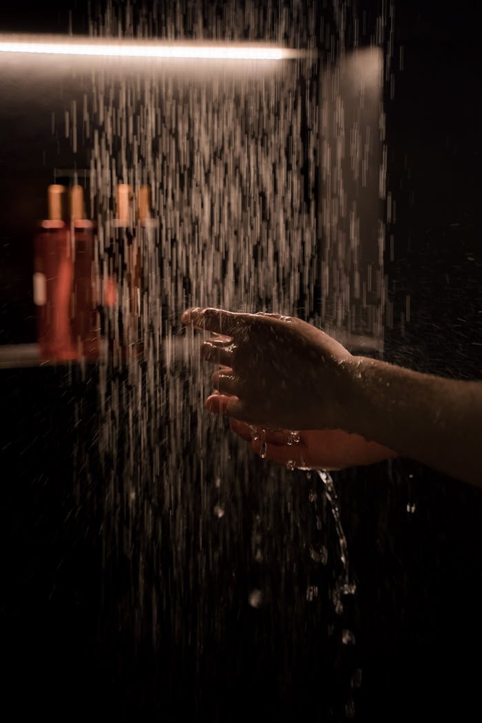 who-we-are-img A tranquil hand under running water in a dimly lit shower setting, capturing moisture and ambiance.