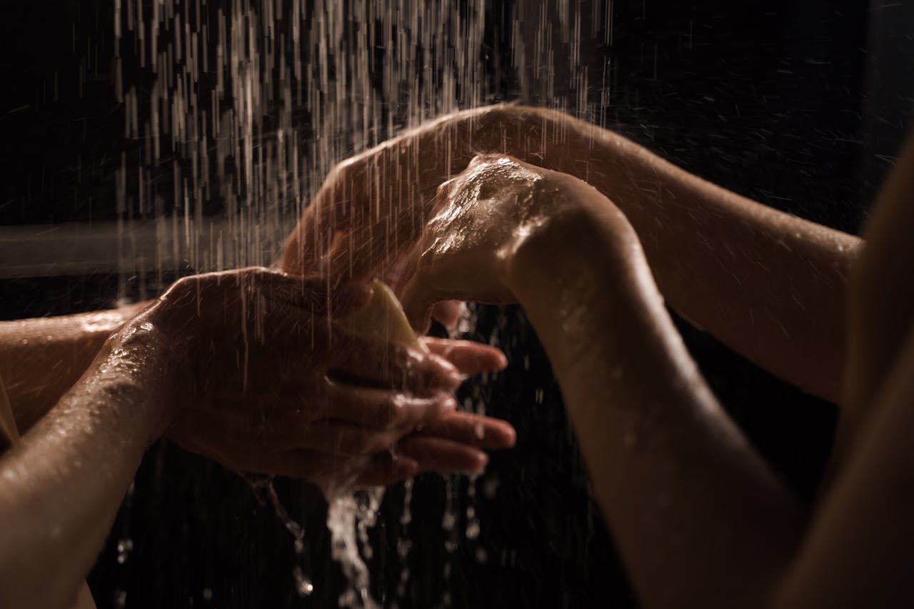 services-03 Close-up of hands washing under a shower, emphasizing cleanliness and care.